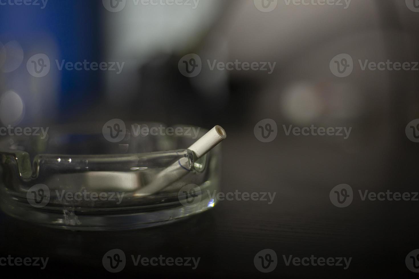 Cigarette in ashtray. Smoking is harmful to health. Glass ashtray on table. photo