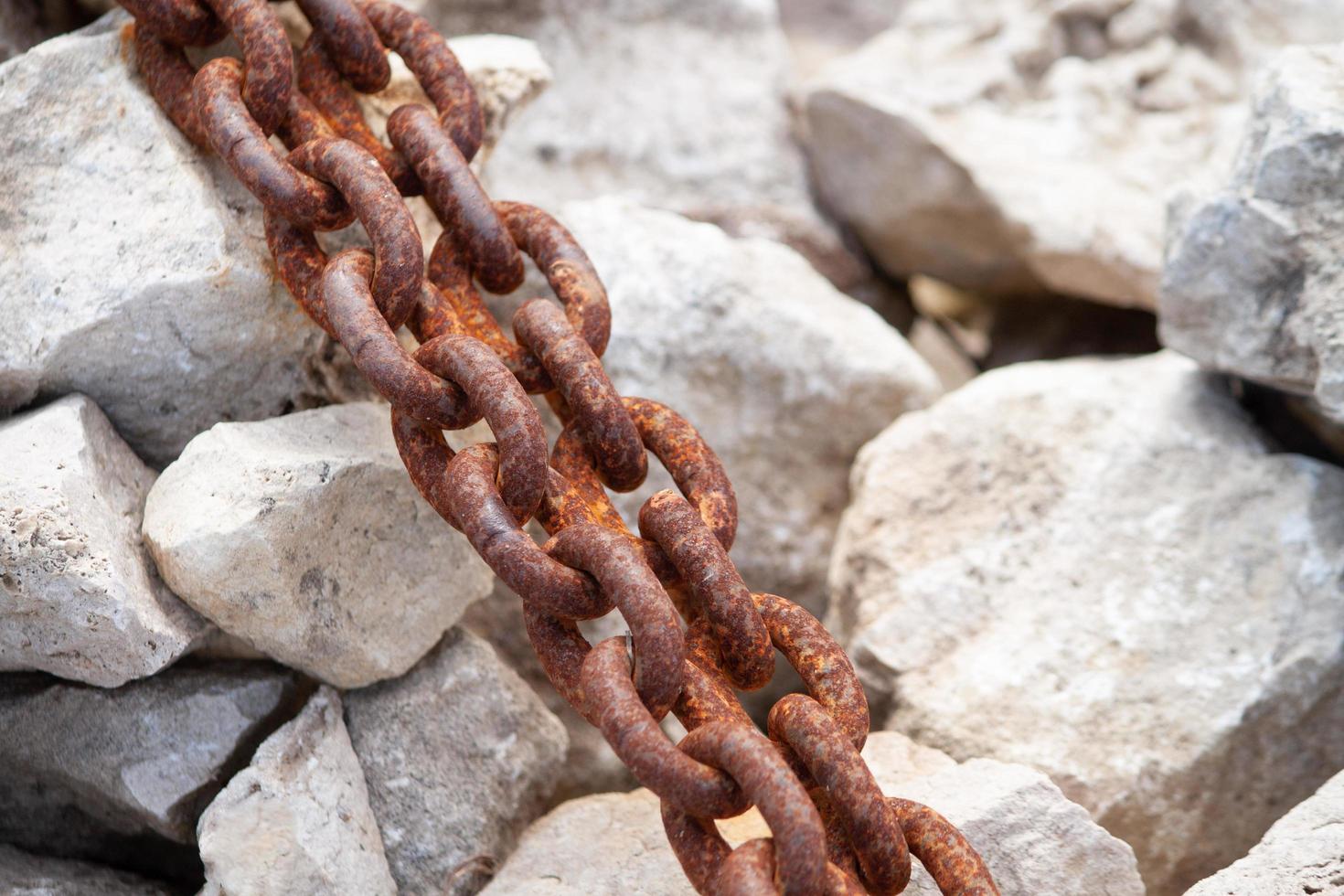 Weathered rusty anchor chain on the white stones of the shoreline. photo
