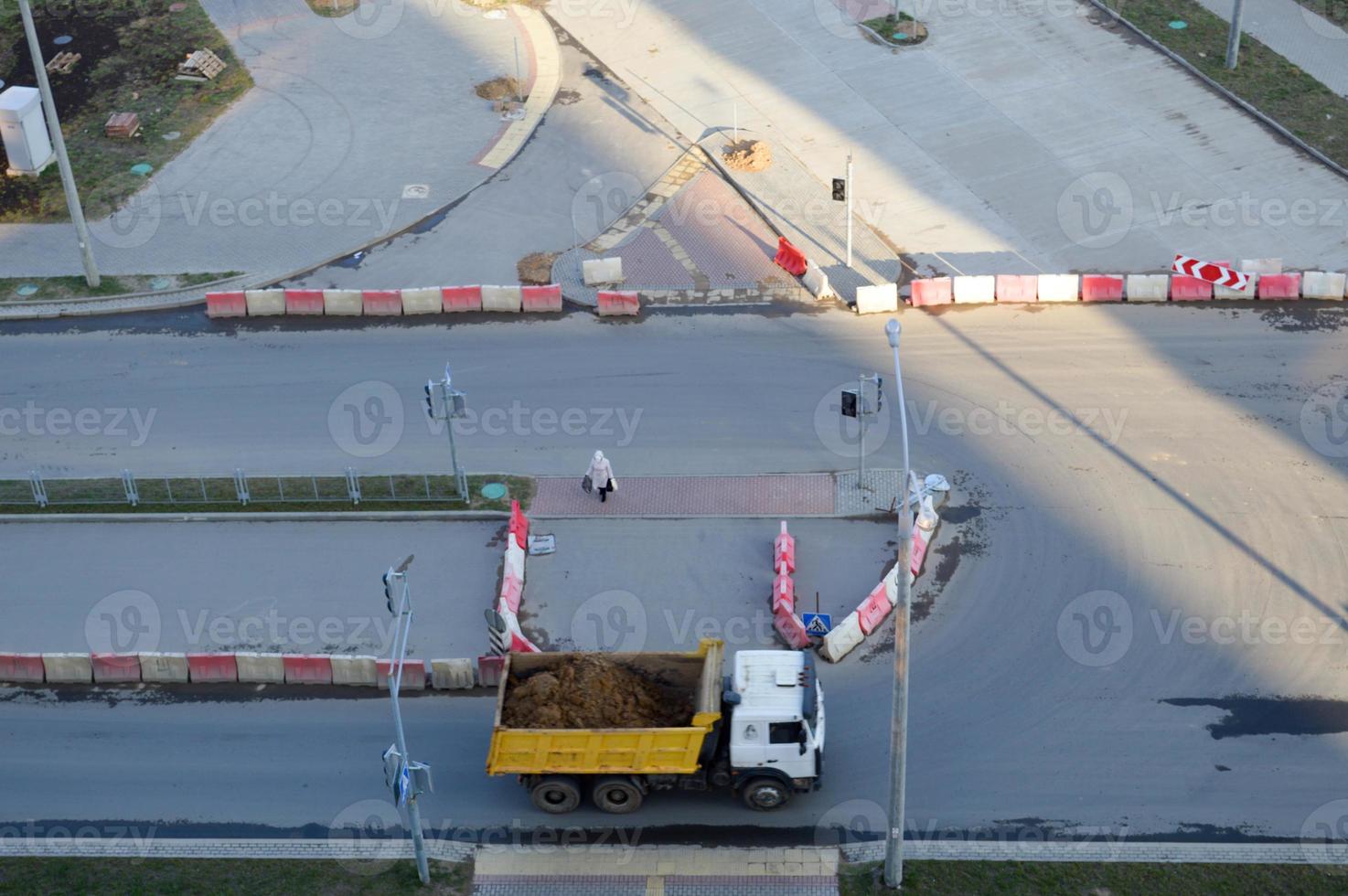 A large dump truck rides to a construction site and carries sand along an asphalt road. View from above photo