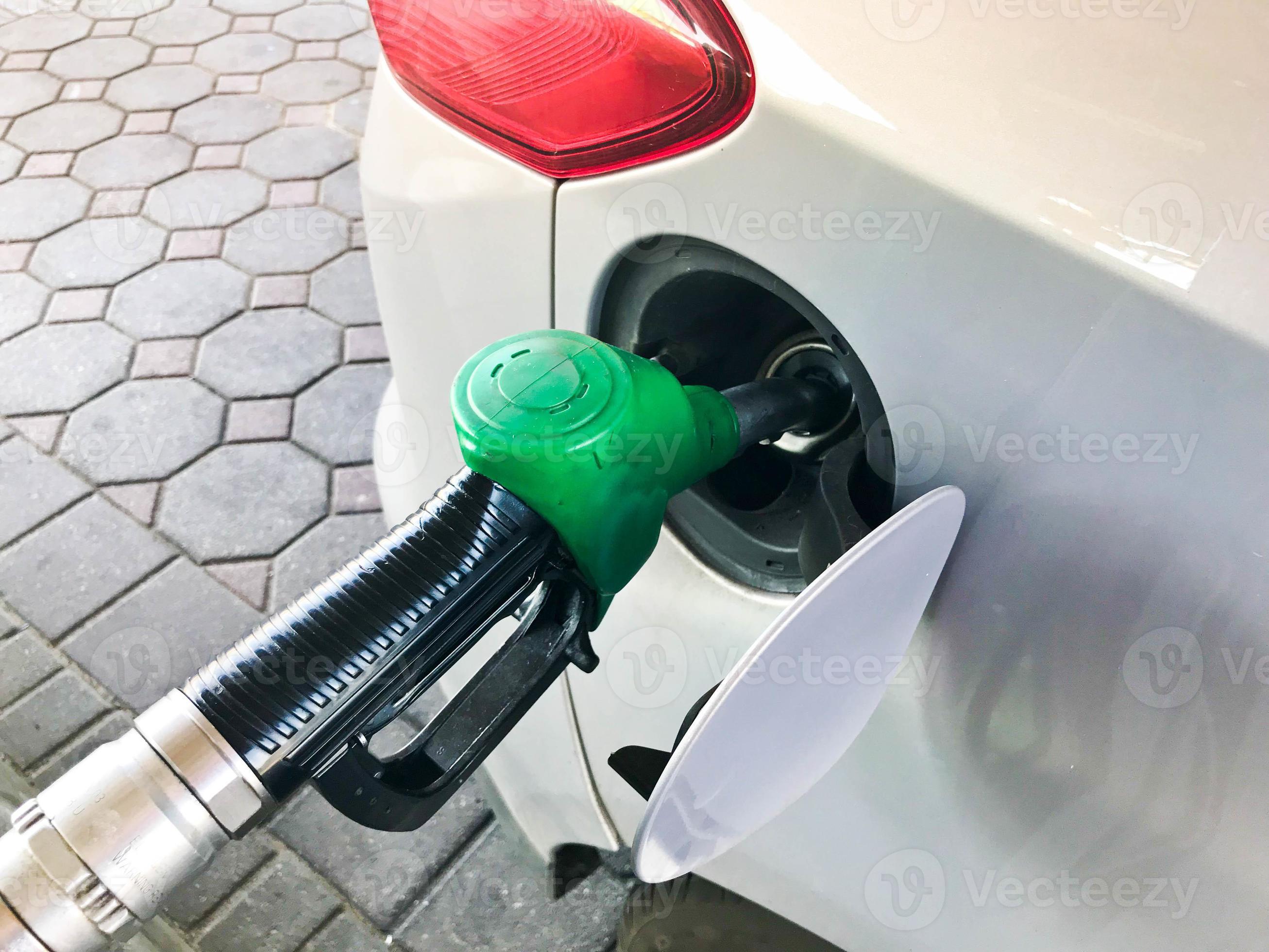 Green filling pistol stuck in the gas tank of a car at a gas station