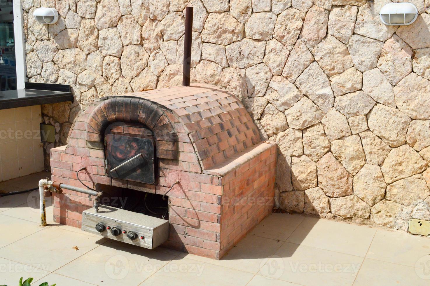 un gran horno industrial profesional de piedra marrón con un tubo para cocinar alimentos fritos de una piedra embaldosada sobre un fondo de pared de piedra en la calle al aire libre foto