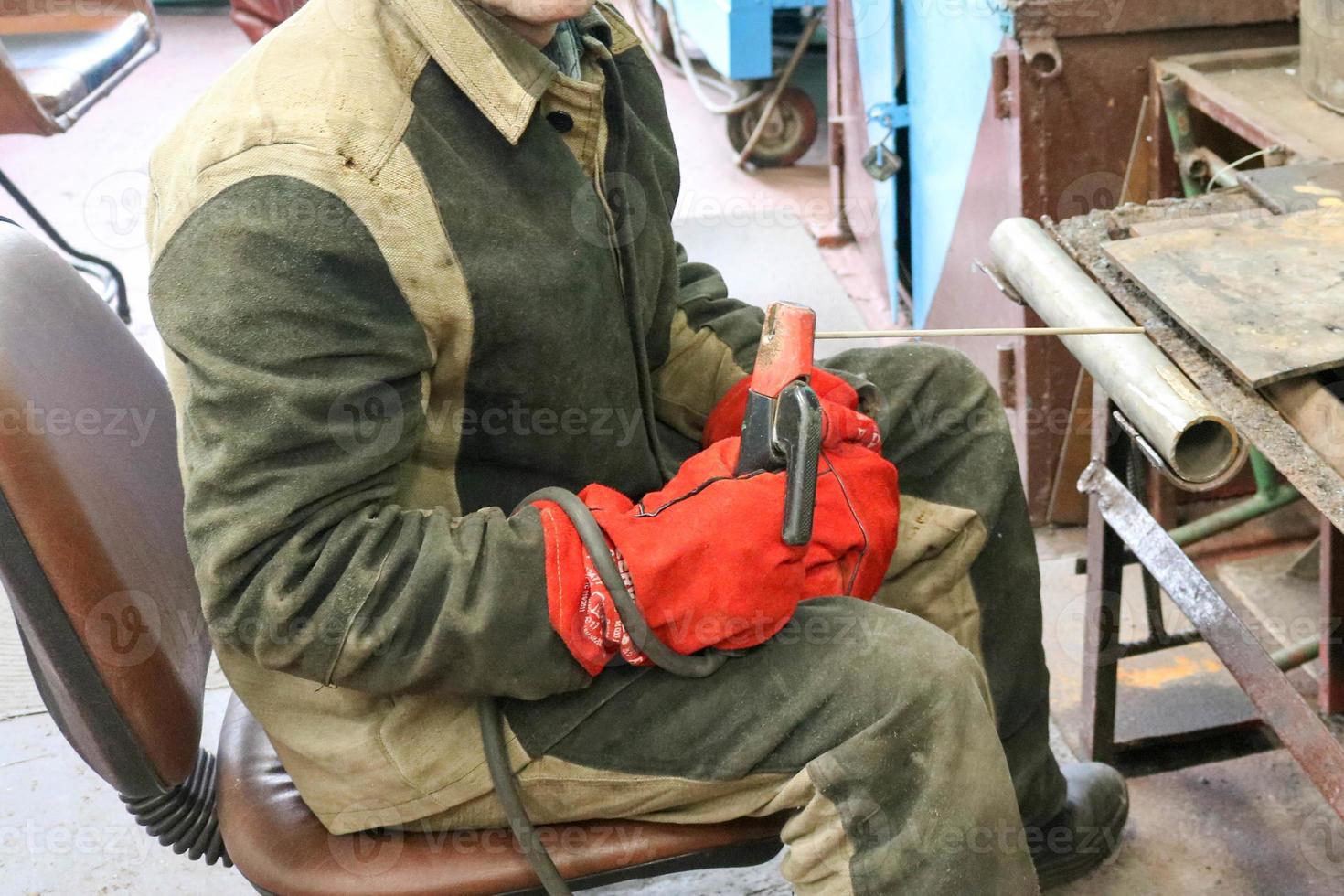 A male worker a welder in a protective mask welds a metal pipe at a welding station in a workshop at a metallurgical plant in a repair facility photo