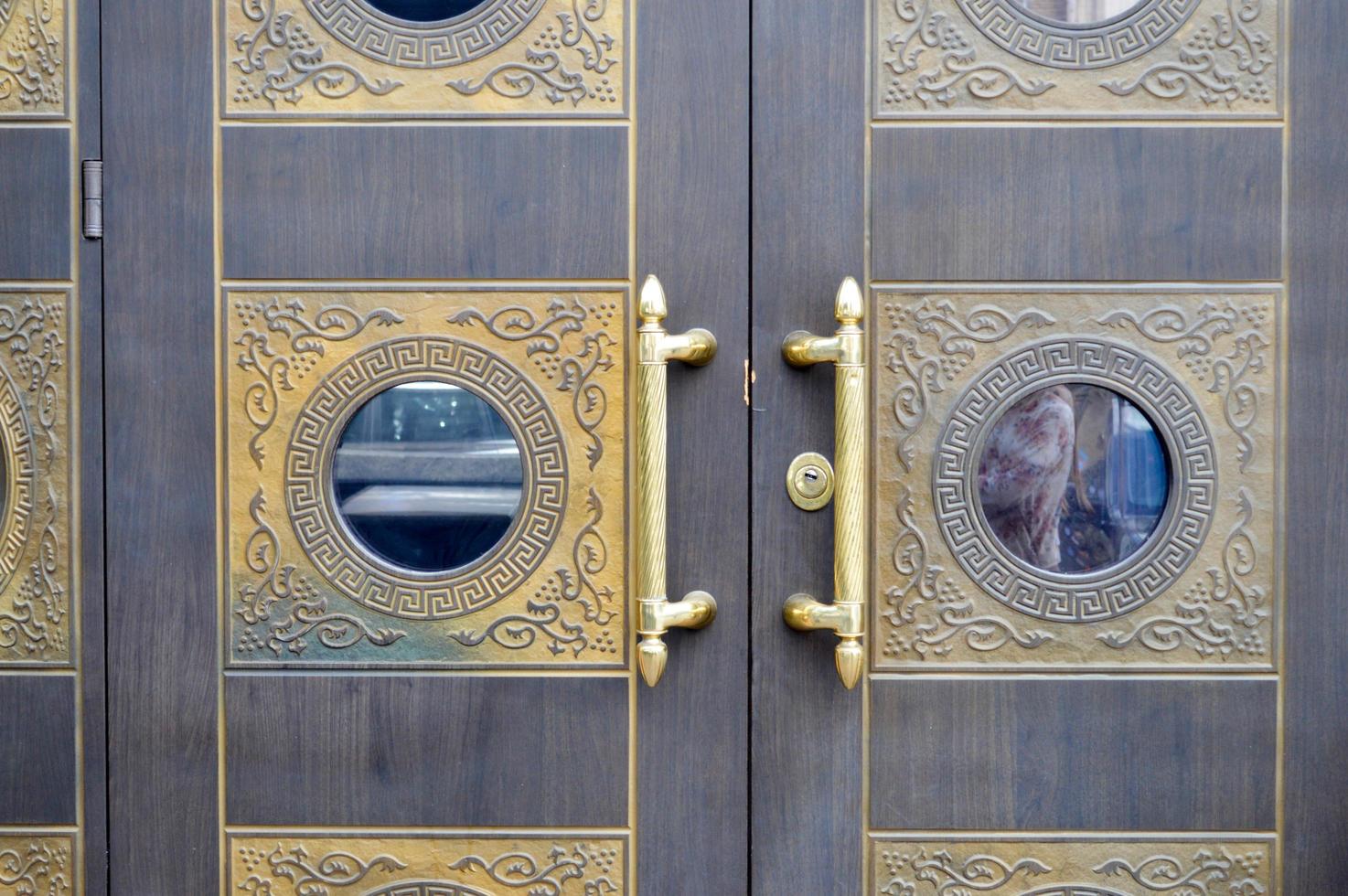 Texture of old decorative beautiful wooden door gates with patterned ornaments and gold ornaments, elements and gold door handles. The background photo