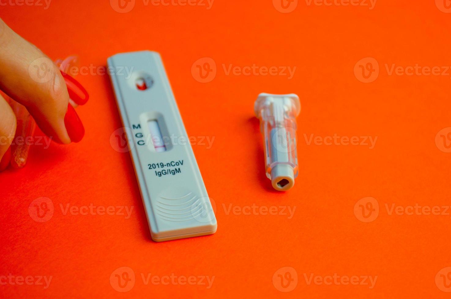 test for coronavirus on an orange background. on a matte background a sensitive strip for coronavirus, a lancet. girl with bright red manicure planning to perform a medical procedure photo