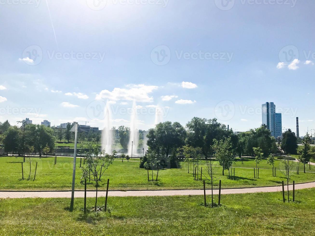 Green beautiful young park in the center of a large city with fountains and seedlings of small trees against the background of buildings photo