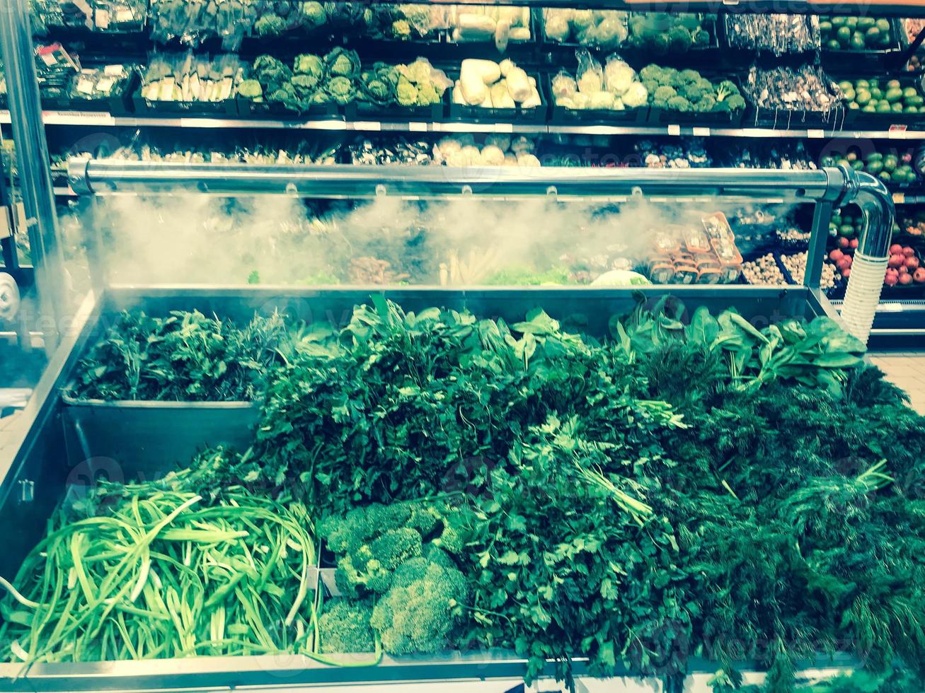 Green fresh environmentally friendly greens of parsley plants dill salad arugula onions and other plant foods lies in a modern refrigerator in a supermarket store on the counter. The background photo