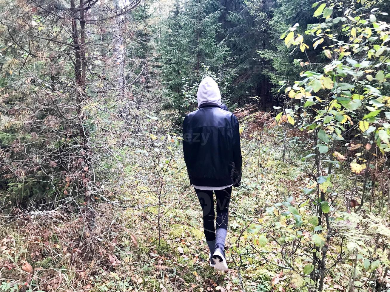 People, mushroom pickers in warm clothes walk in a hike through the autumn forest with trees in the nature along the grass and leaves photo