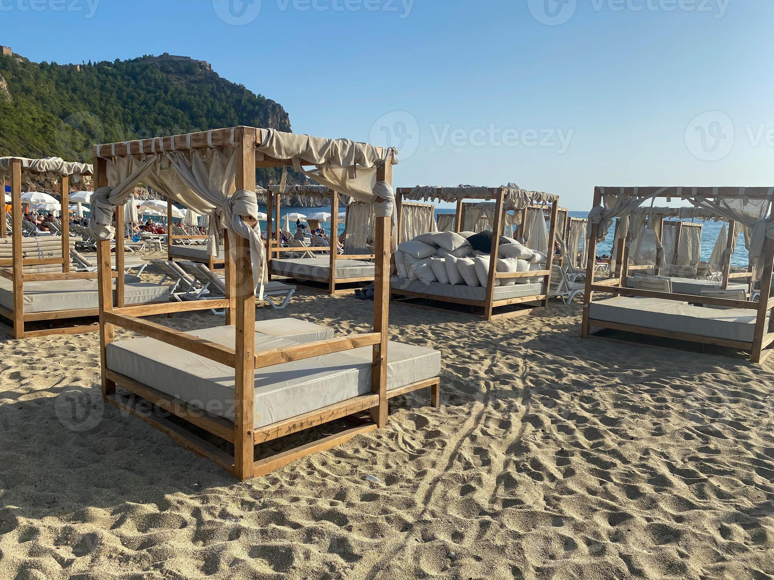 Many sunbeds and canopies on a sandy beach with a mountain and sea in a