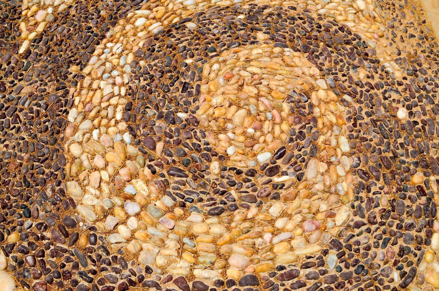 The texture of the stone wall, the road from small round and oval stones with abstracted lines of spiral patterns with sandy seams of natural old yellow black brown. The background photo