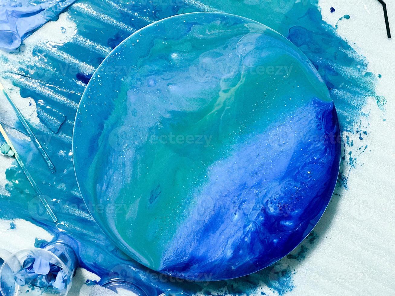 The process of creating a home-made trendy abstract modern pattern painted with a brush of acrylic blue multi-colored resin on a round wooden board photo