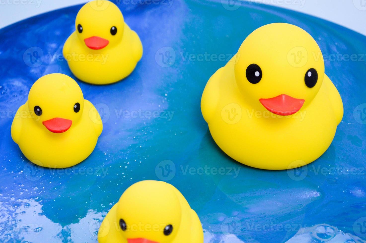 patos de goma amarillos flotando en la superficie del océano de epoxi. los juguetes decorativos se colocan en una imagen interior brillante en forma de agua con reflejos solares. fondo abstracto foto