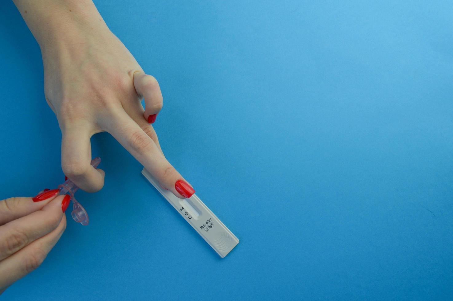 blood test for the diagnosis of coronavirus. a girl with a bright red manicure applies a finger with a drop of blood after a puncture for an express test. sensitive strip for detecting coronavirus photo