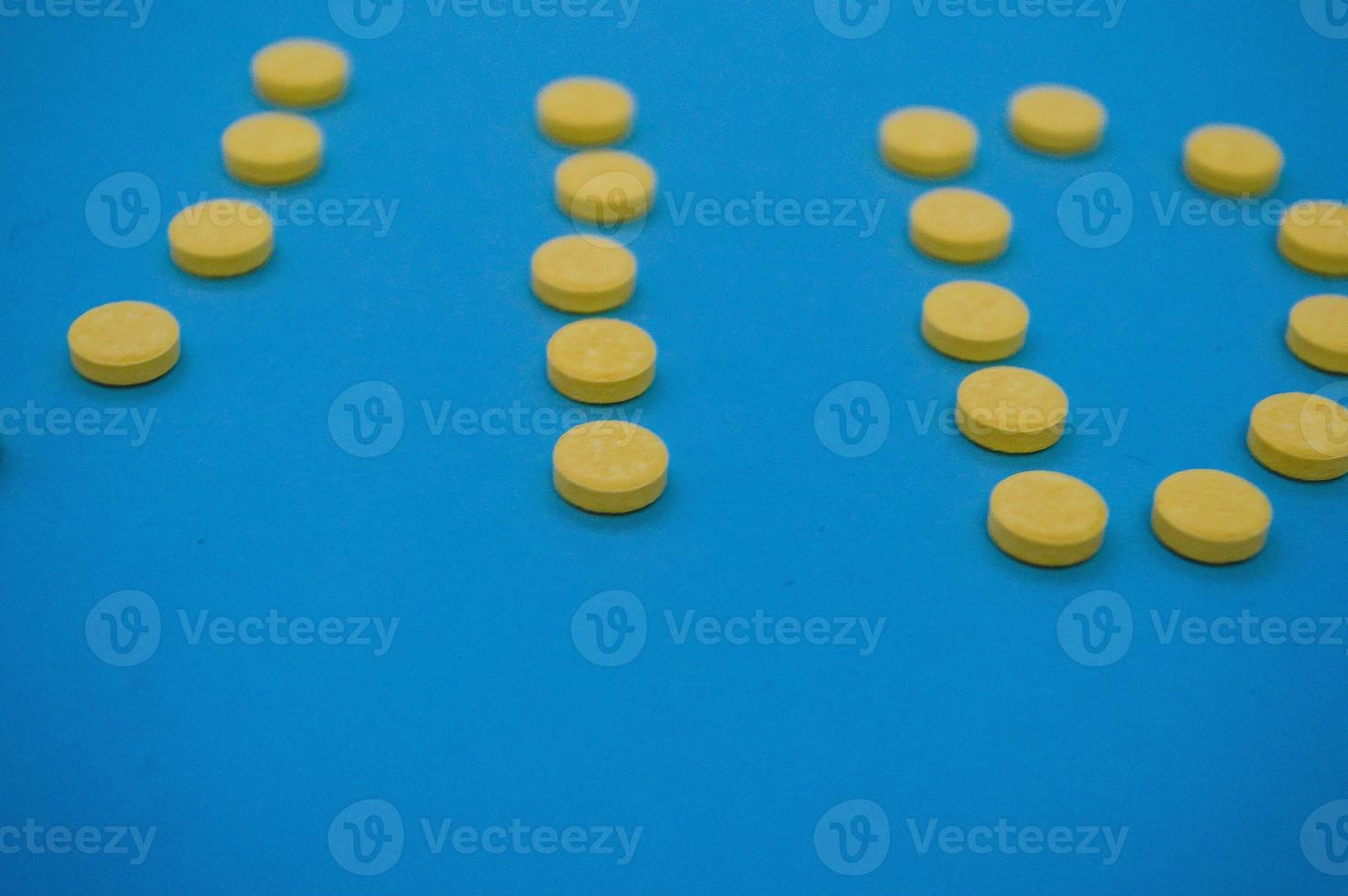 volumetric yellow pills shot on a blue background in the form of letters. medicines poured from a can are shot from above on colored backgrounds. English alphabet in the form of tablets photo