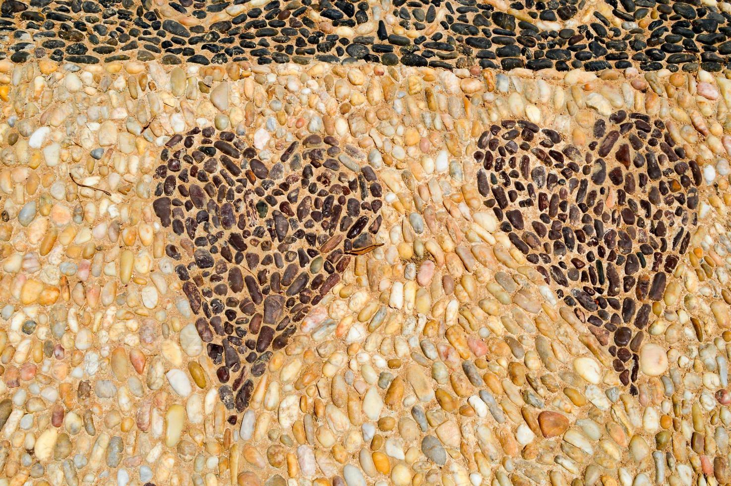The texture of the stone wall, the road from small round and oval stones with abstracted lines of patterns of two hearts sandy seams of natural old yellow black brown. The background photo