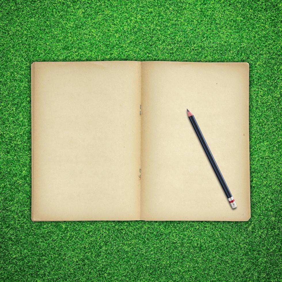 Pencil and old book open on green grass background photo