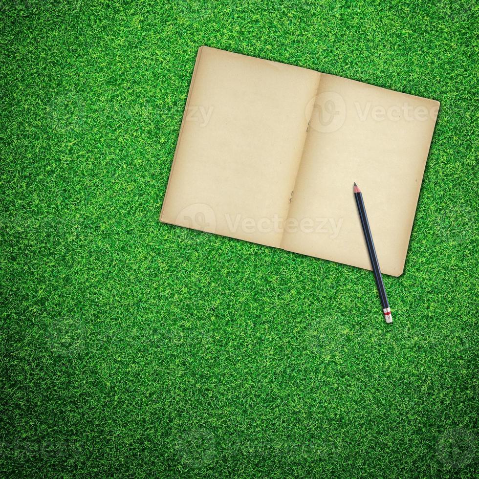 Pencil and old book open on green grass background photo