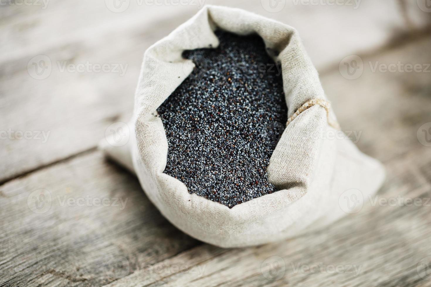 semillas de amapola en una bolsa de arpillera sobre un fondo gris de madera vintage. las semillas sabrosas y útiles ricas en proteínas y aceites. foto