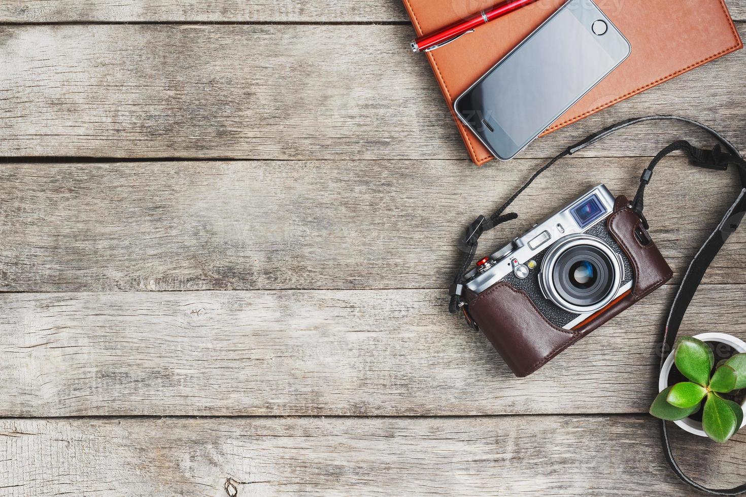 Classic camera with a brown organizer red pen on a gray wooden, vintage desk with a telephone and green growth. The concept of the list for the photographer in travels. Free space in country style photo