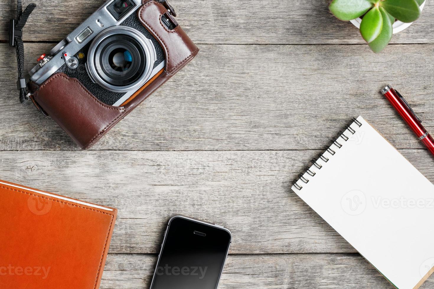 Classic camera with blank notepad page and red pen on gray wooden, vintage table with telephone and green flower. Brown notebook. photo