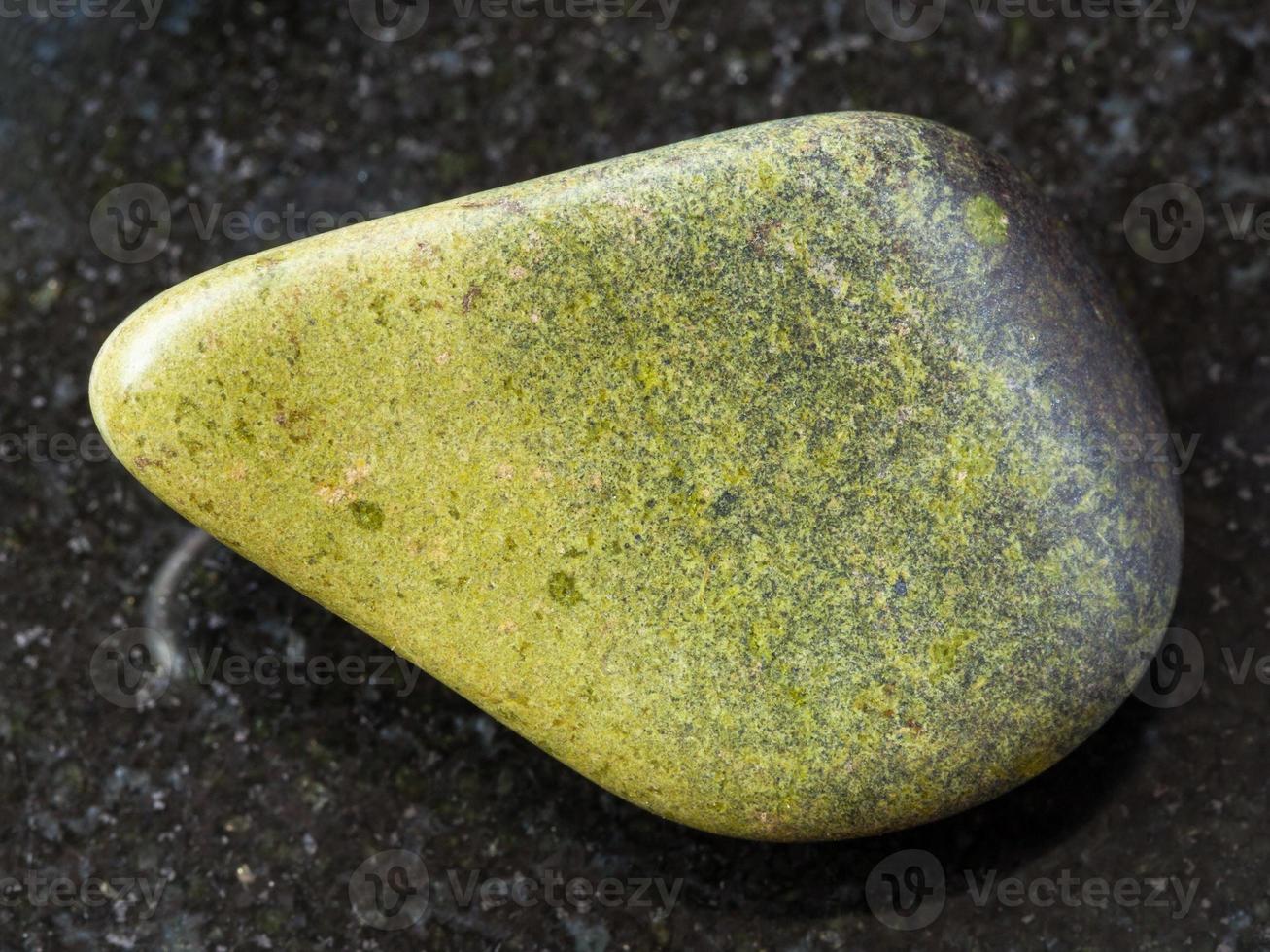 tumbled epidote gemstone on dark background photo