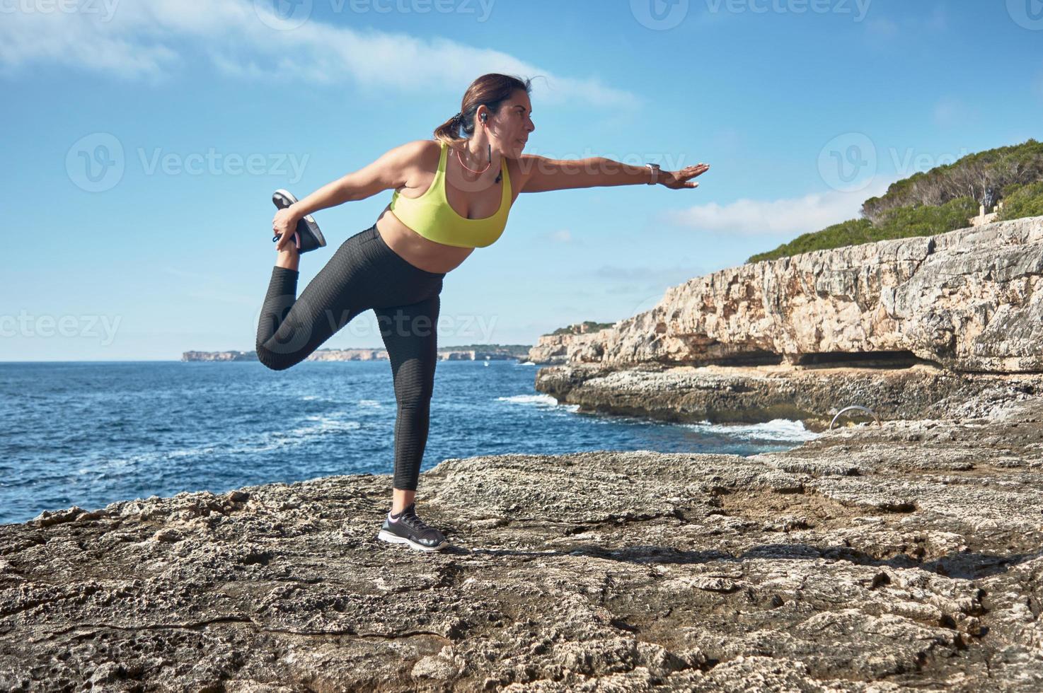 Latin woman, middle-aged, wearing sportswear, training, doing physical exercises, plank, sit-ups, climber's step, burning calories, keeping fit, outdoors by the sea, wearing headphones, smart watch photo