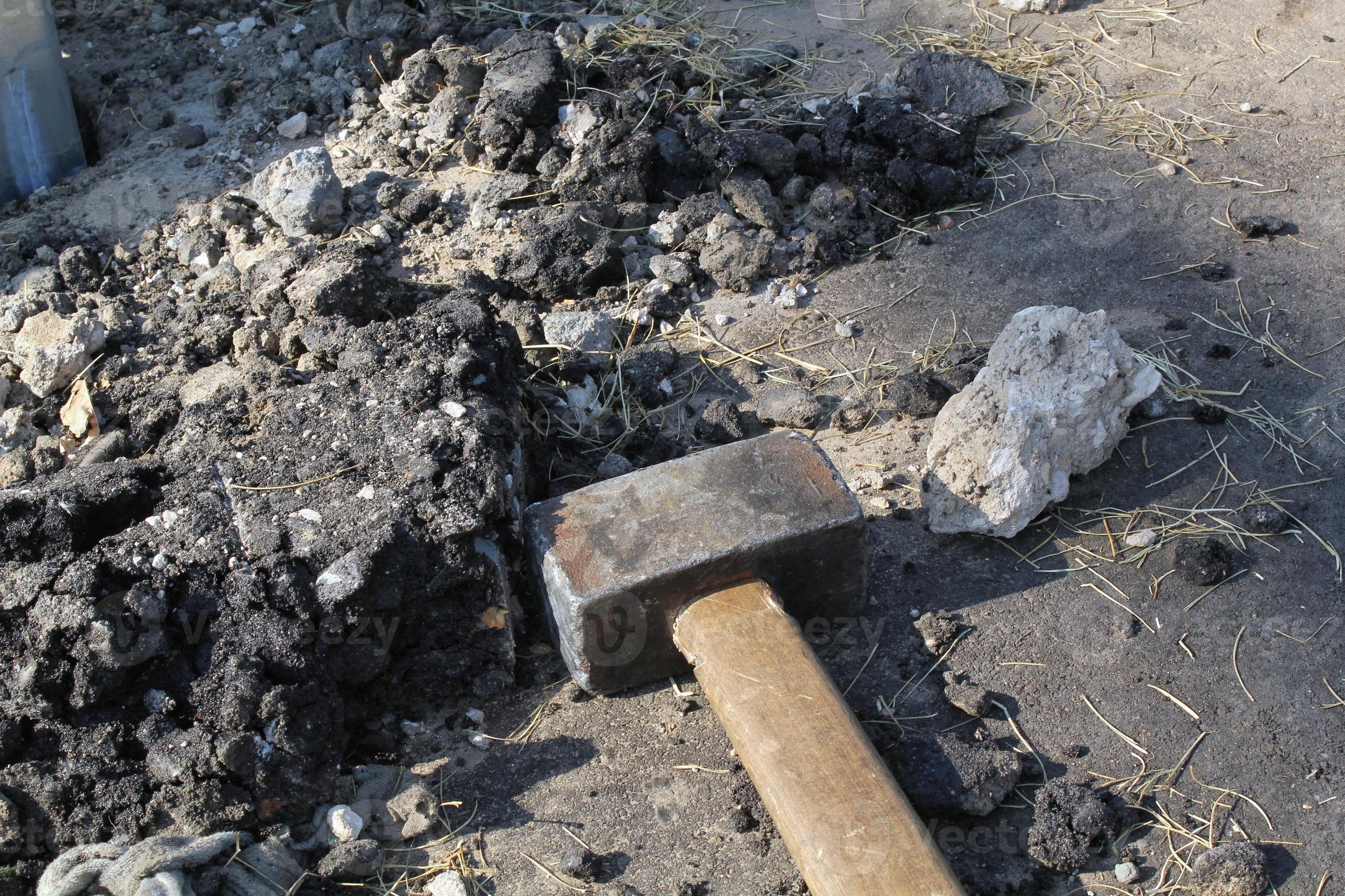Closeup of big metal steel sledge hammer with wooden handle on cracking old pavement after road