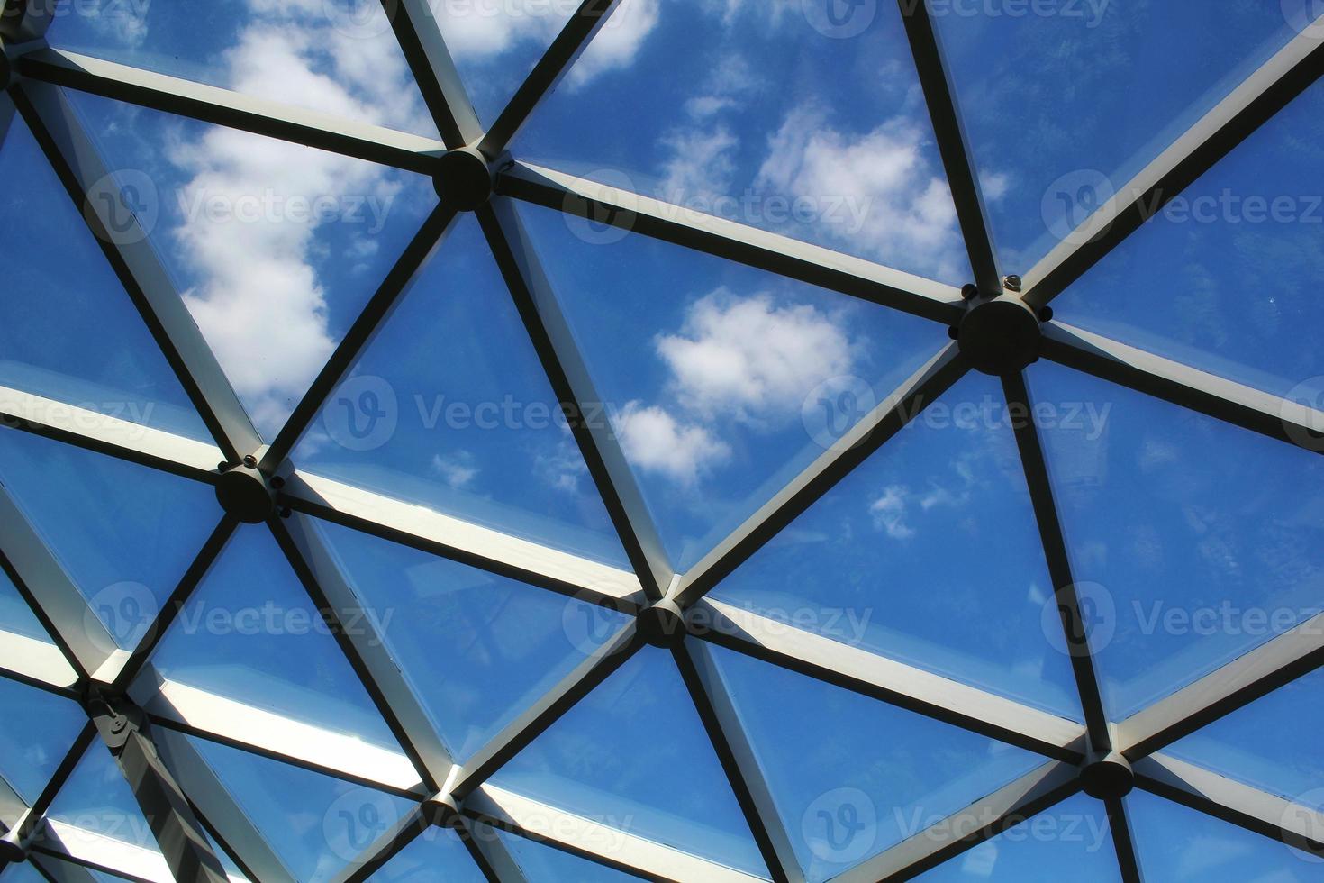 Transparent glass dome roof of modern design style pavilion building with geometric metal construction pattern. View of blue sky and clouds. Abstract structure triangle high-tech architecture window. photo