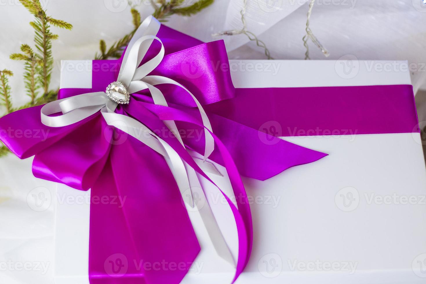 A Christmas gift decorated with a beautiful bow on a light background with a twig, if. Selective focus. the concept of Christmas and New Year. photo