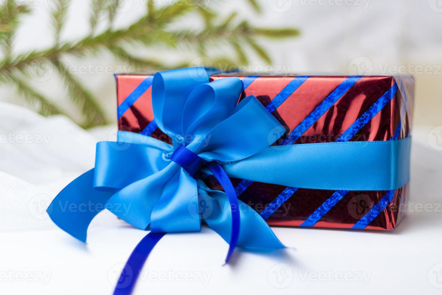 A Christmas gift decorated with a beautiful bow on a light background with a twig, if. Selective focus. the concept of Christmas and New Year. photo