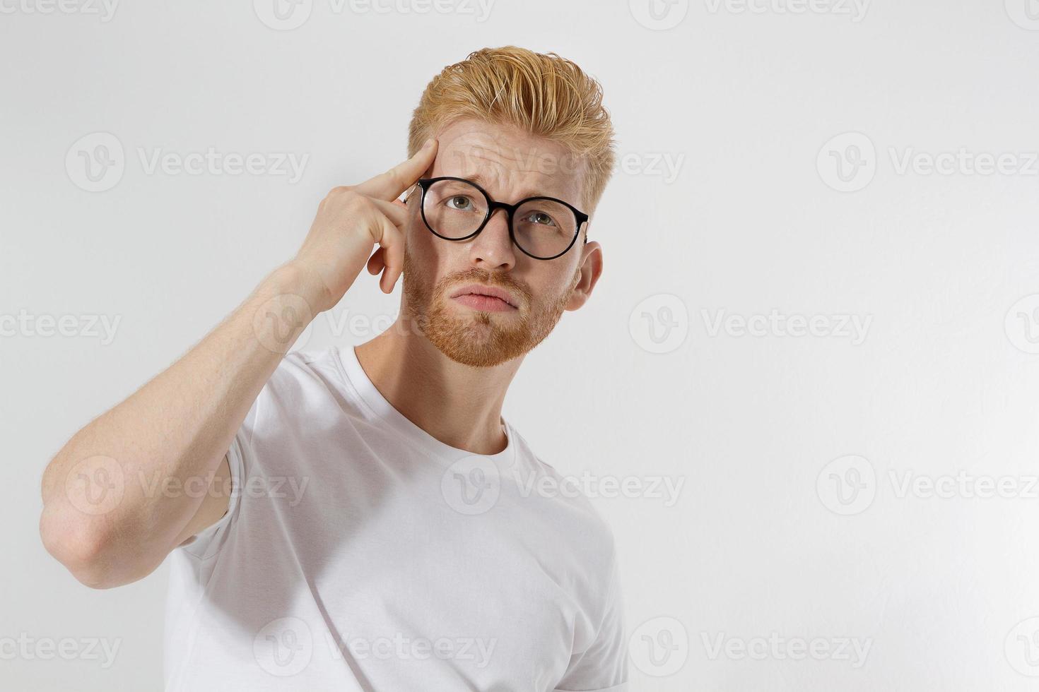 Young man in thinking process. Close up redheaded guy with red beard in white t shirt, glasses focus on creating startup idea isolated on gray background. Intellect mind and brain power. Mental health photo