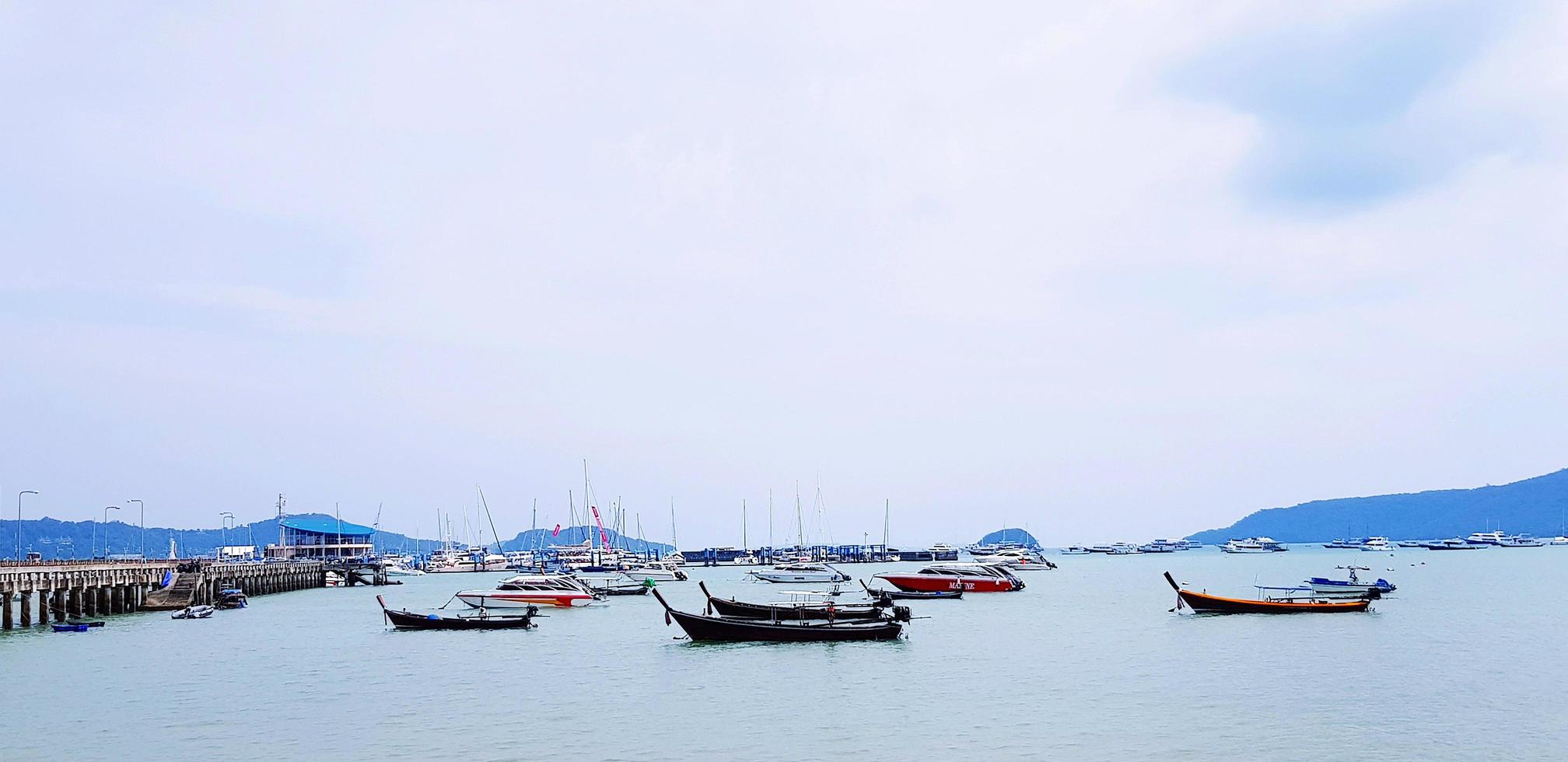 Many long tail boat and speed boat on the sea at port. Vehicle on ocean with blue sky and white cloud background with copy space on top or above. Landscape of view at Phuket, Thailand. Travel and Trip photo