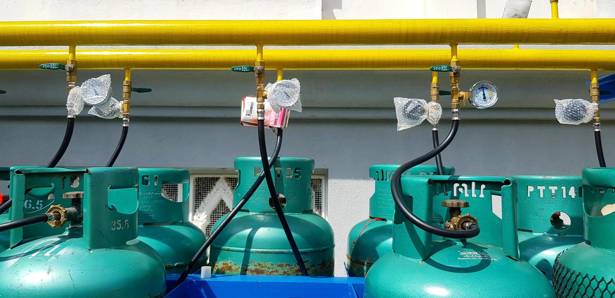 bangkok, tailandia - 5 de marzo de 2022 grupo de nuevos tanques de gas verde instalados con valor, tubería o tubería amarilla y fondo de pared blanca. Objeto para hacer fuego para cocinar alimentos en la cocina. foto