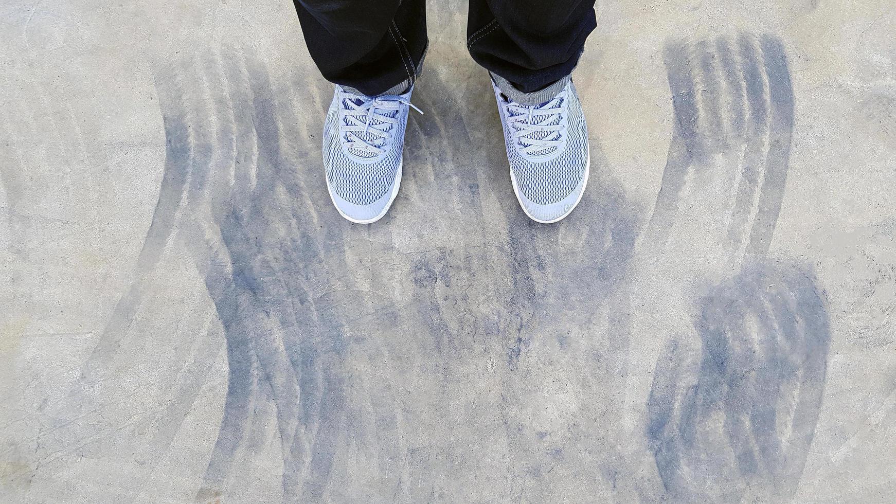 Top view of leg wearing blue jeans and gray or grey sneakers or fashion shoes on floor with car wheel or brake mark on road or street with copy space. Flat lay of part body. Abstract background photo