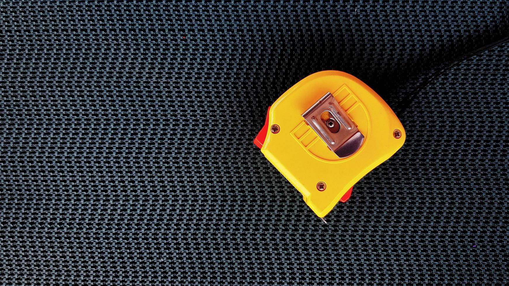 Yellow Tape measure on black conveyor belt background with copy space on left. Tool for  measure distance of object and size or dimension. photo