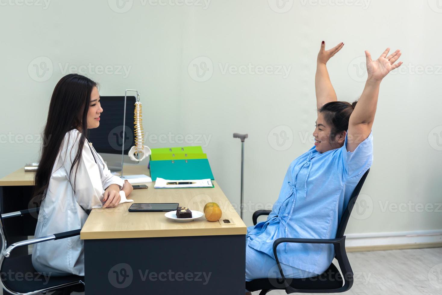 Overweight  Asia woman raised hands and discussing test results with female doctor in hospital, Frozen shoulder concept. photo