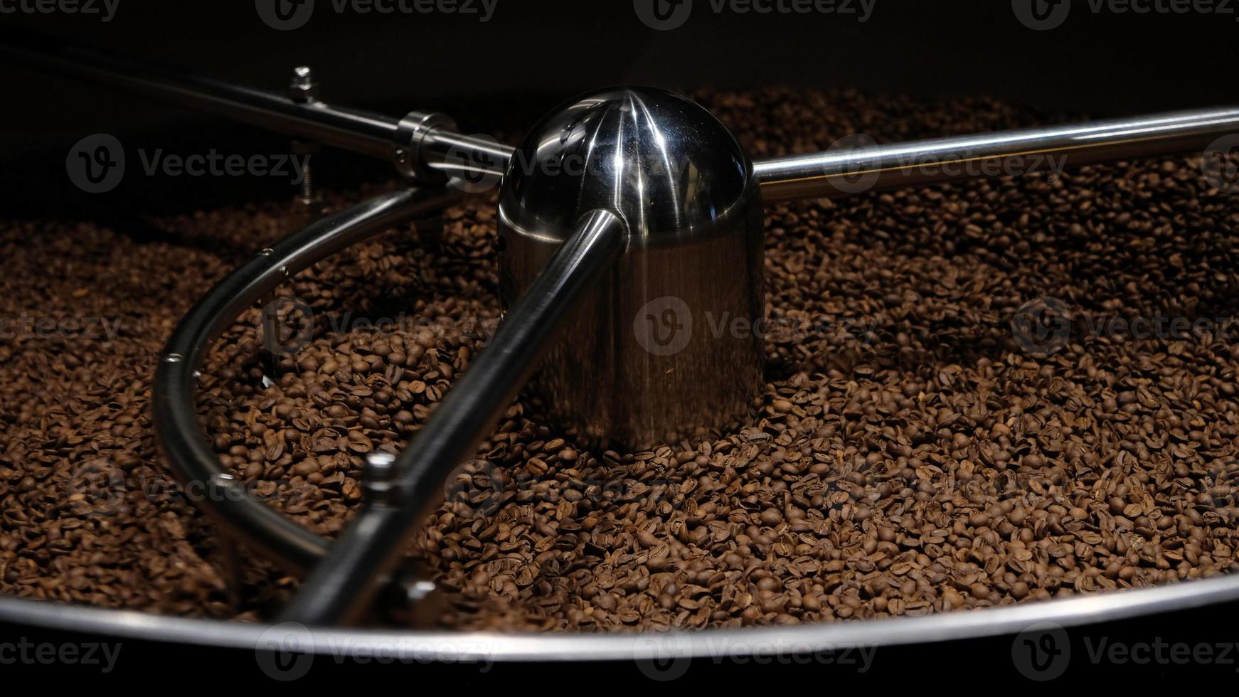 Coffee roaster machine at coffee roasting process. Mixing coffee beans. Roasted spinning cooler professional machines and fresh brown coffee beans movement close-up dark photo at factory.