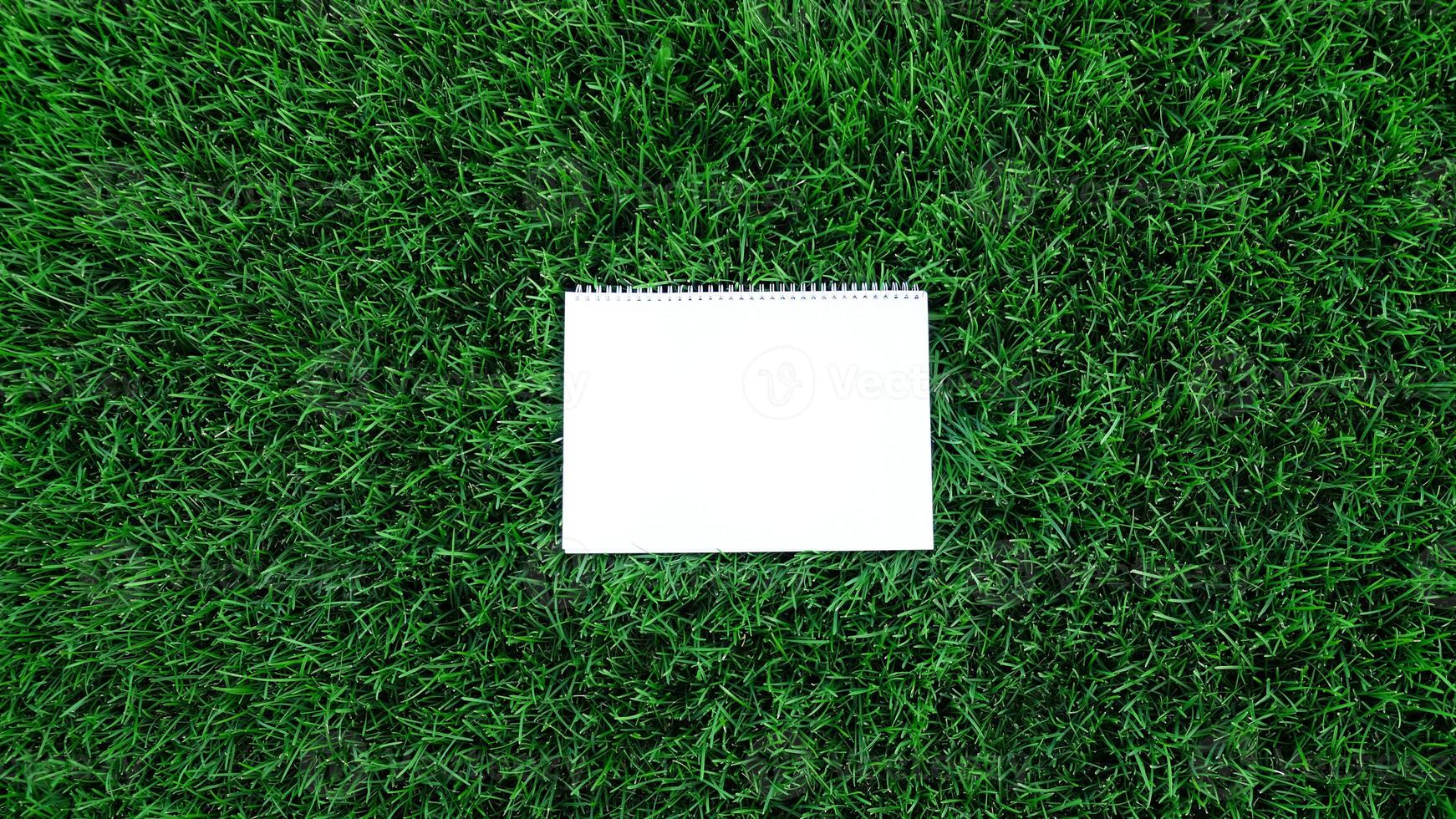 Empty white paper on green grass background. For message flat lay with copy space for text or products presentation. Nature concept, business and lifestyle environment. photo