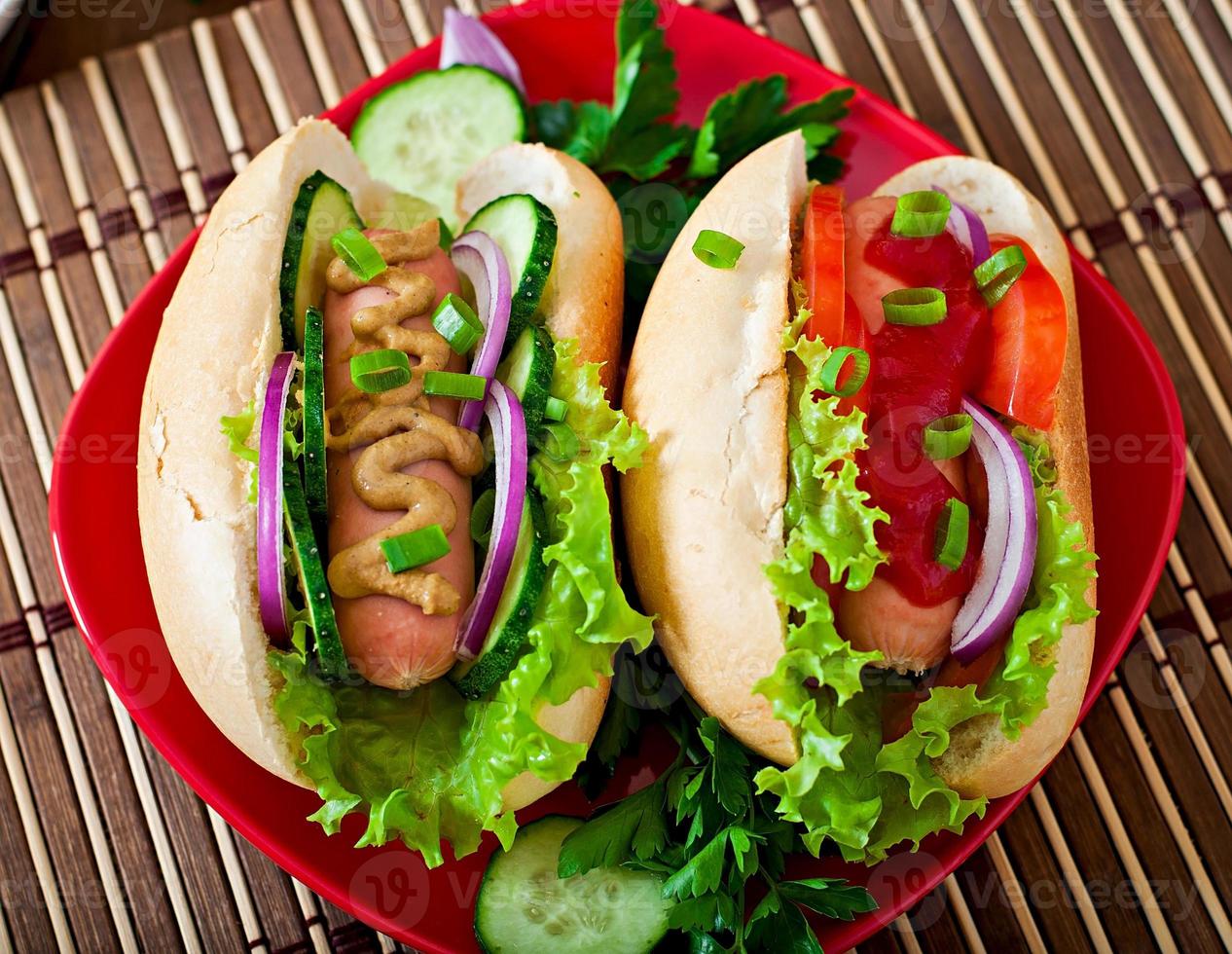 Hotdog with ketchup, mustard, lettuce and vegetables on wooden table photo