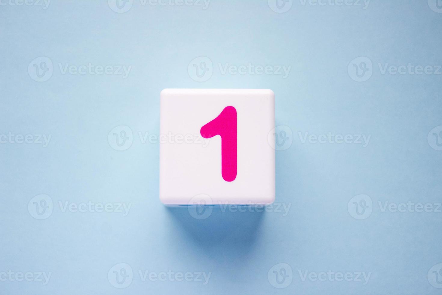 Close-up photo of a white plastic cube with a pink number 1 on a blue background. Object in the center of the photo