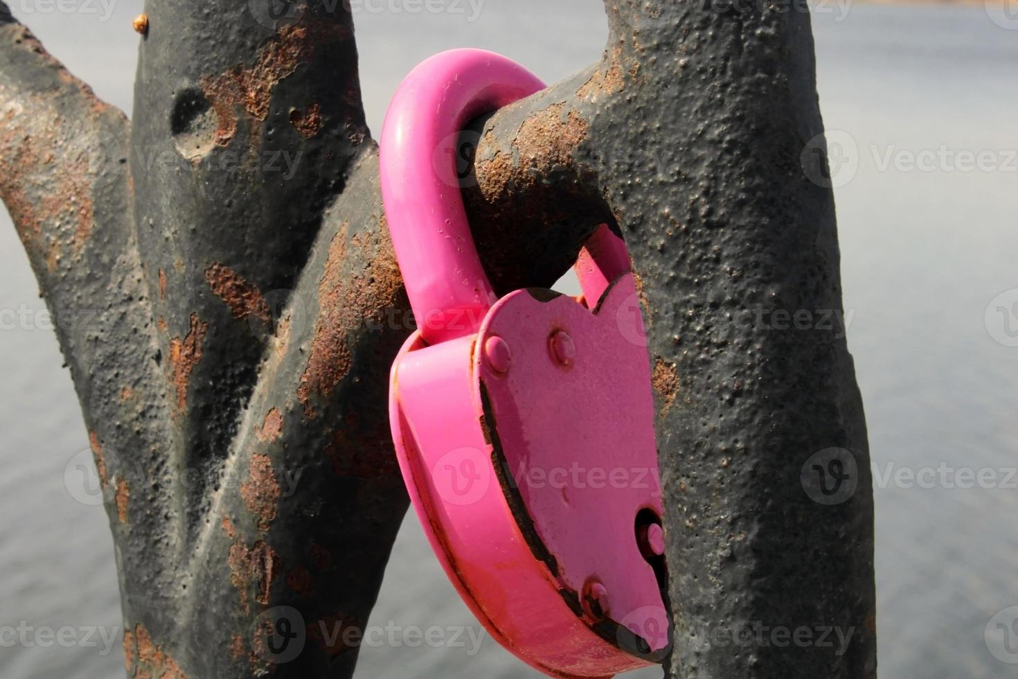 un candado rosa en forma de corazón cuelga de una celosía oxidada. tradición nupcial. el concepto de amor y fidelidad foto