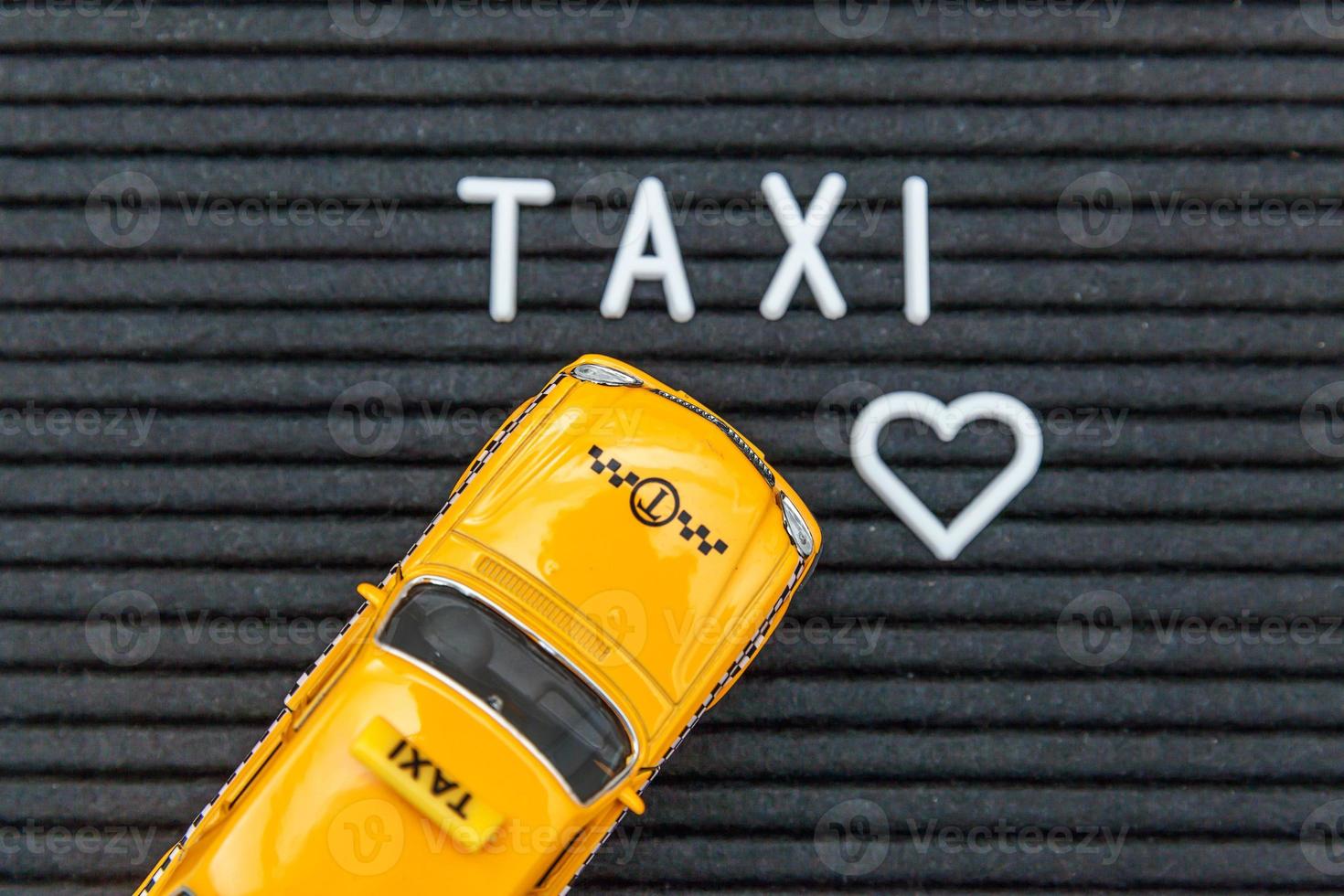 Simply design yellow toy car Taxi Cab model with inscription TAXI letters word on black background. Automobile and transportation symbol. City traffic delivery urban service idea concept. Copy space. photo