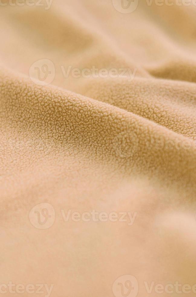 The blanket of furry orange fleece fabric. A background of light orange soft plush fleece material with a lot of relief folds photo