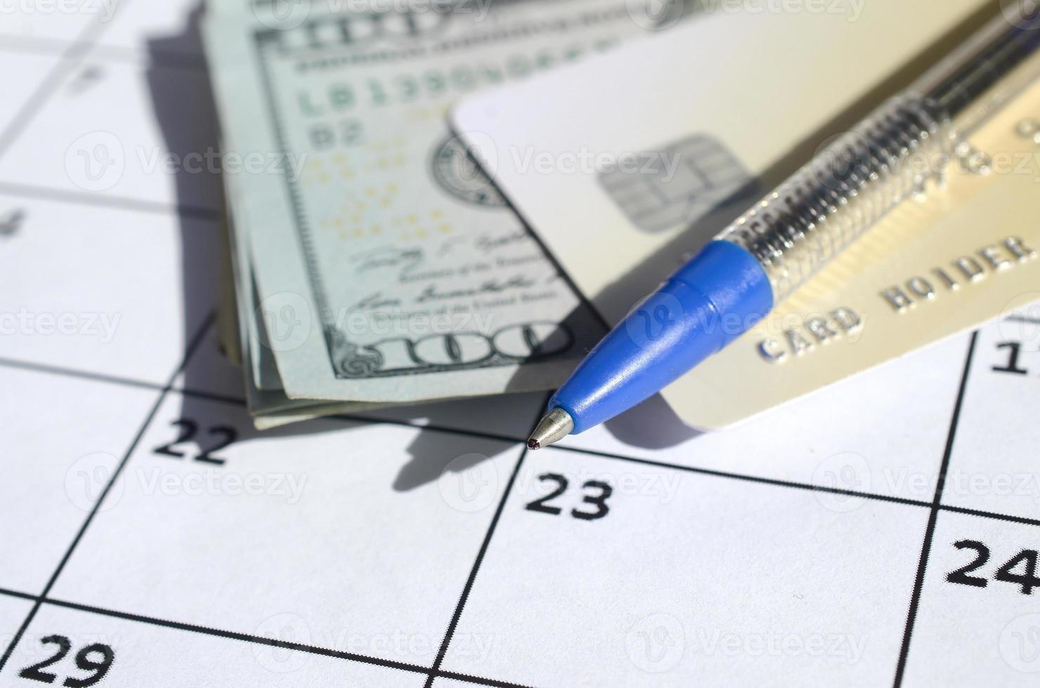 Pen and credit card on many hundred US dollar bills on calendar page close up photo