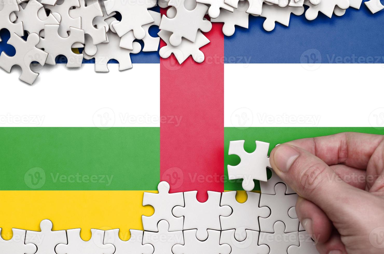 Central African Republic flag  is depicted on a table on which the human hand folds a puzzle of white color photo