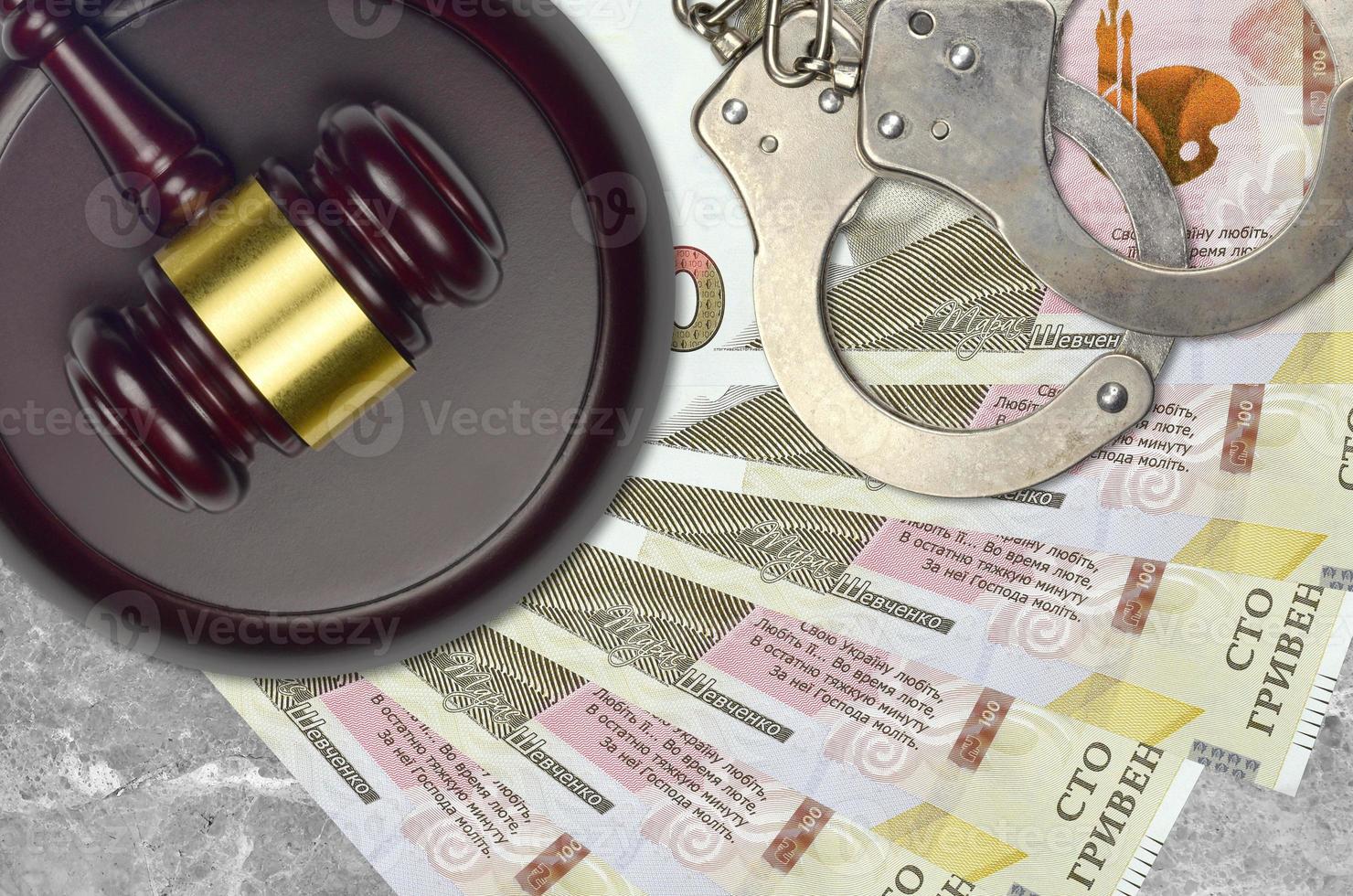 100 Ukrainian hryvnias bills and judge hammer with police handcuffs on court desk. Concept of judicial trial or bribery. Tax avoidance photo