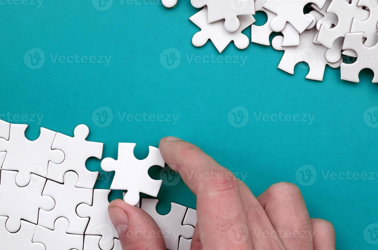 The hand folds a white jigsaw puzzle and a pile of uncombed puzzle pieces lies against the background of the blue surface. Texture photo with space for text