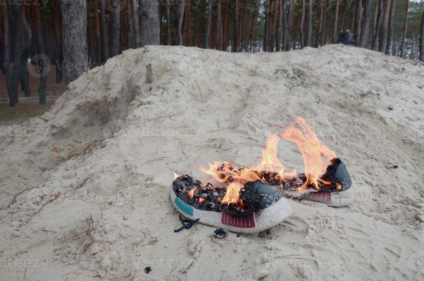 Burning sports sneakers or gym shoes on fire stand on sandy beach coast. Athlete burned out. Physical exertion during training concept photo