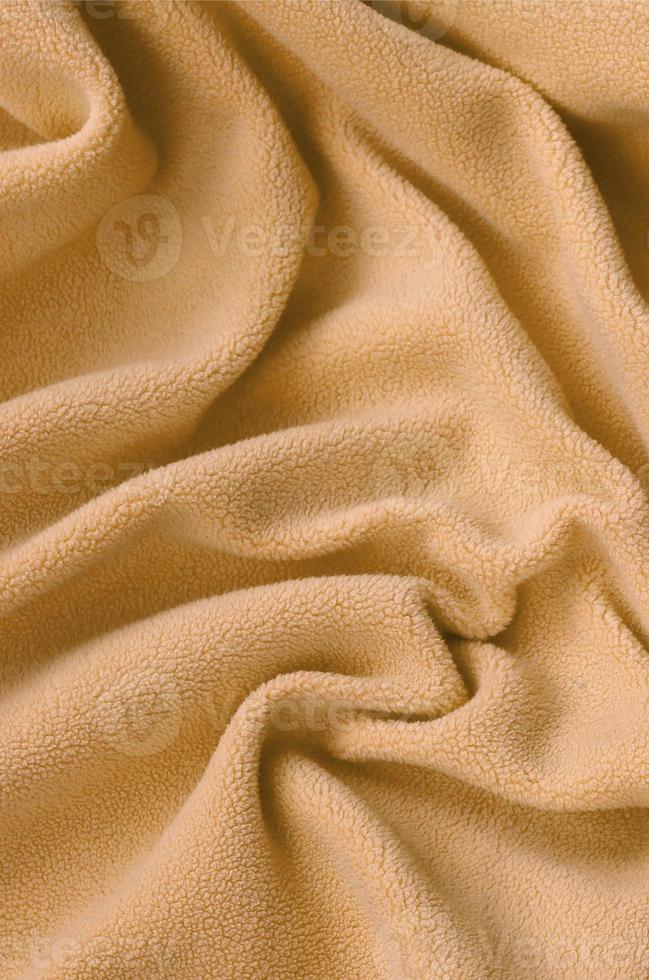 The blanket of furry orange fleece fabric. A background of light orange soft plush fleece material with a lot of relief folds photo