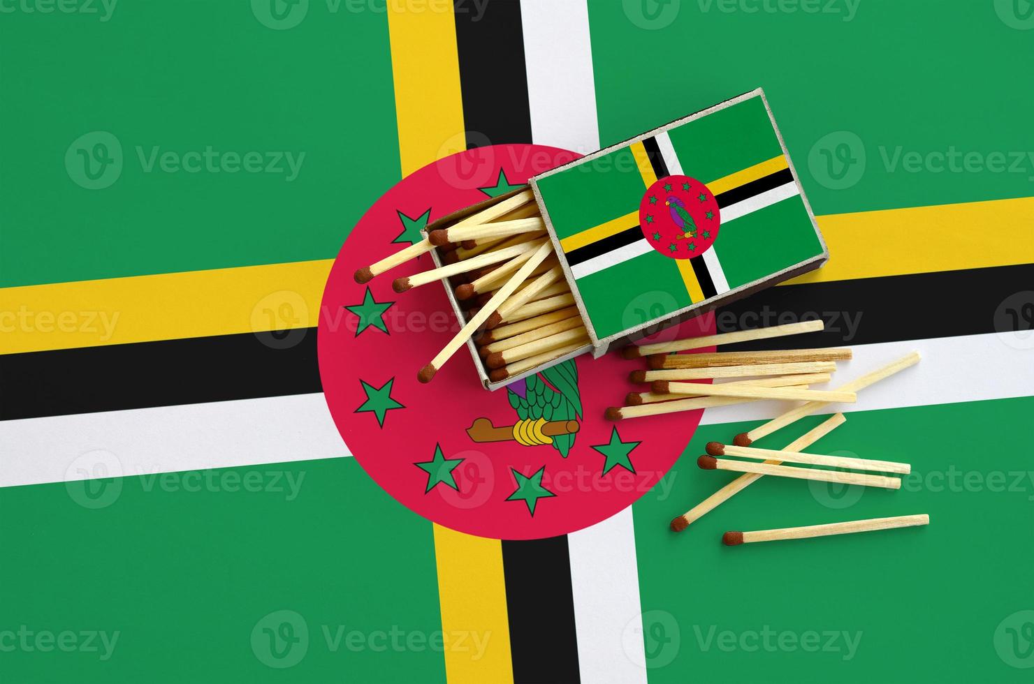 Dominica flag  is shown on an open matchbox, from which several matches fall and lies on a large flag photo
