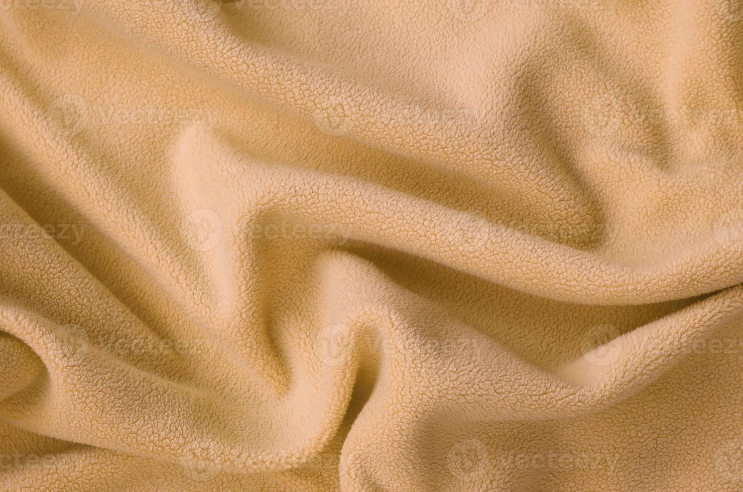 The blanket of furry orange fleece fabric. A background of light orange soft plush fleece material with a lot of relief folds photo